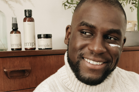 A black man with clear skin promoting skincare products for black men and haircare